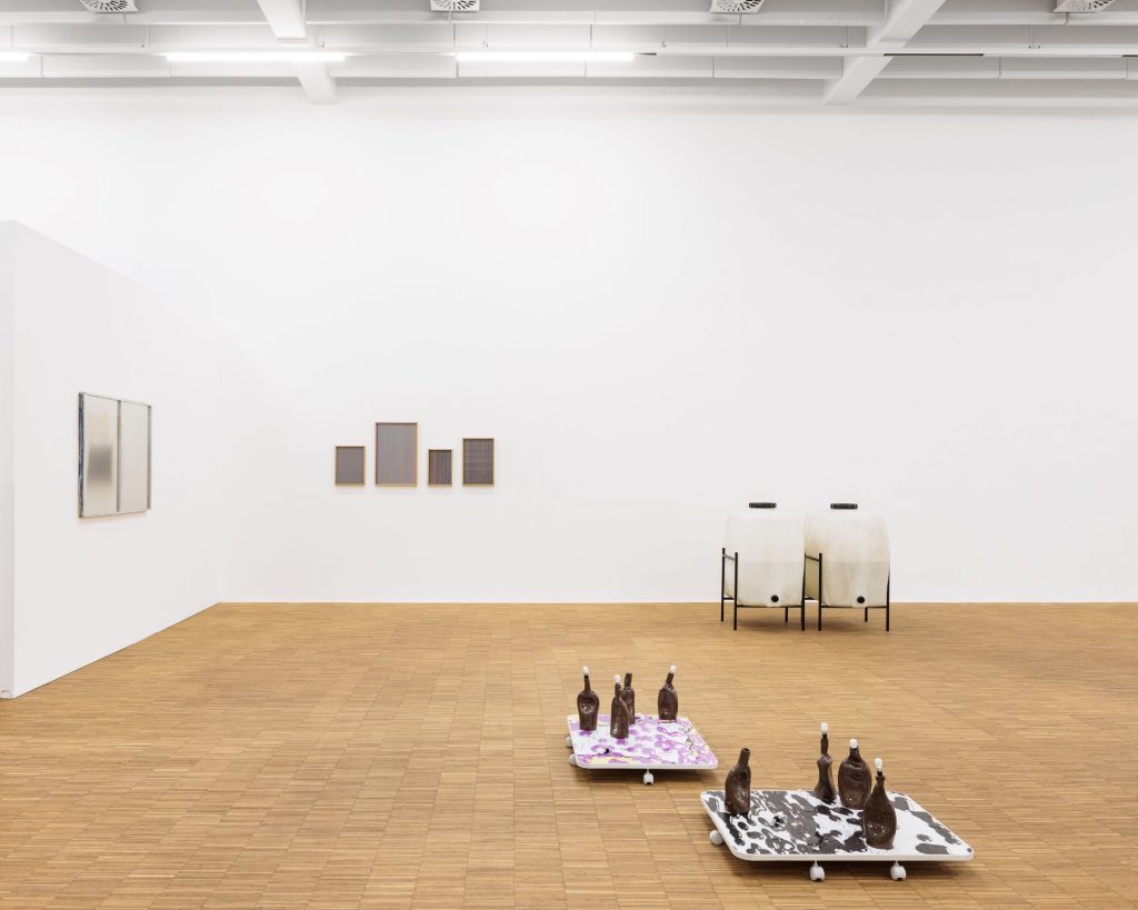 Blick in die Ausstellung „vakuum“ mit Arbeiten von Francisco Valença Vaz und Martin Sommer: deformierte Tonflaschen auf bunten Platten, dahinter zwei Lithiumbehälter vor weißer Wand