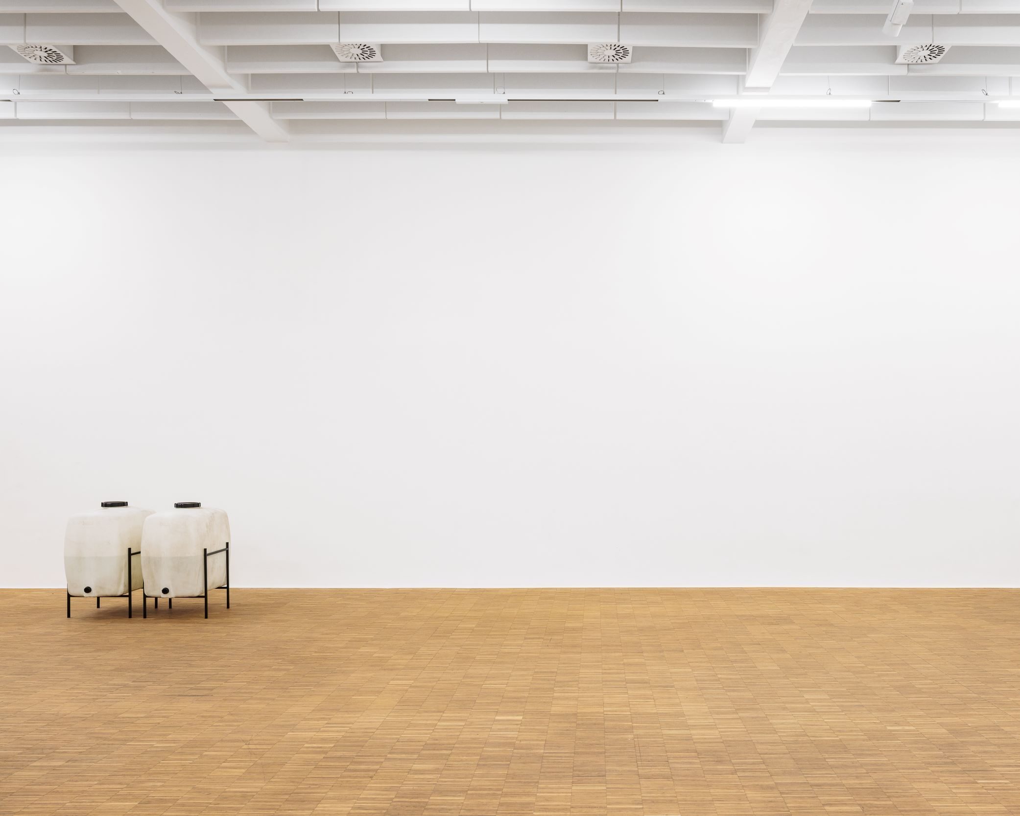 Zwei weiße Kunststoffkanister in Metallgestellen stehen im leeren Ausstellungsraum der vakuum Ausstellung im Salzburger Kunstverein
