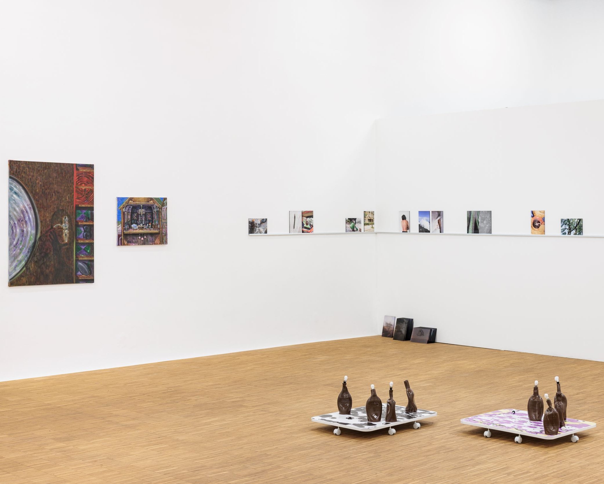 Blick in die Ausstellung vakuum im Salzburger Kunstverein mit zwei Ölgemälden von Ani Gurashvili an der linken Wand und zwei Podesten mit deformierten Tonflaschen auf farbigen Bildplatten von Francisco Valença Vaz im Vordergrund