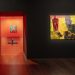 Ein Gemälde in einem dunklen Raum und eine Tür in einen zweiten Ausstellungsraum