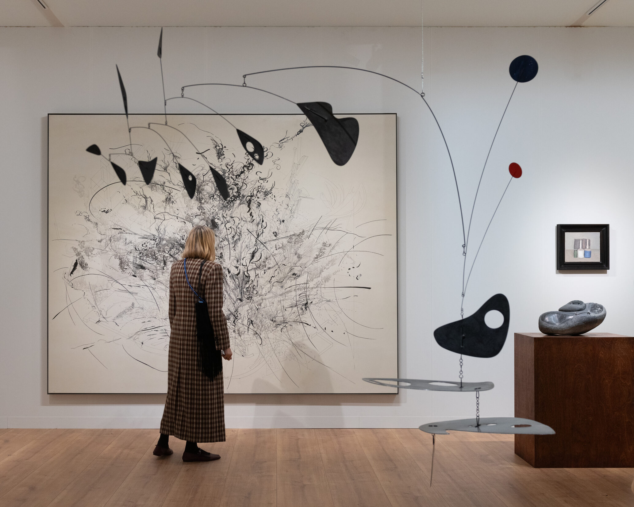 Besucherin vor großformatiger abstrakter Tuschezeichnung auf einer Kunstmesse in Paris, umgeben von schwarzen Mobiles von Alexander Calder und Skulpturen auf Holzsockeln
