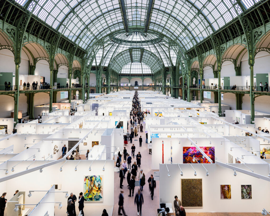 Blick von oben auf die Kunstmesse Art Basel Paris im Grand Palais: Messestände mit Gemälden unter der historischen Glas-Stahl-Kuppel, Besucher im Mittelgang